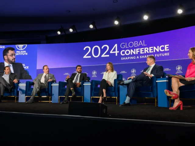 Six panelists sit on stage at the Milken Global Conference 2024, engaging in a "Thriving in Disruption" discussion. Dana Settle joins the conversation, with a large purple event banner displayed behind them.